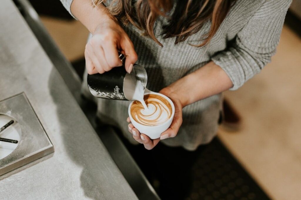 Barista schenkt melk in een kop koffie met latte art