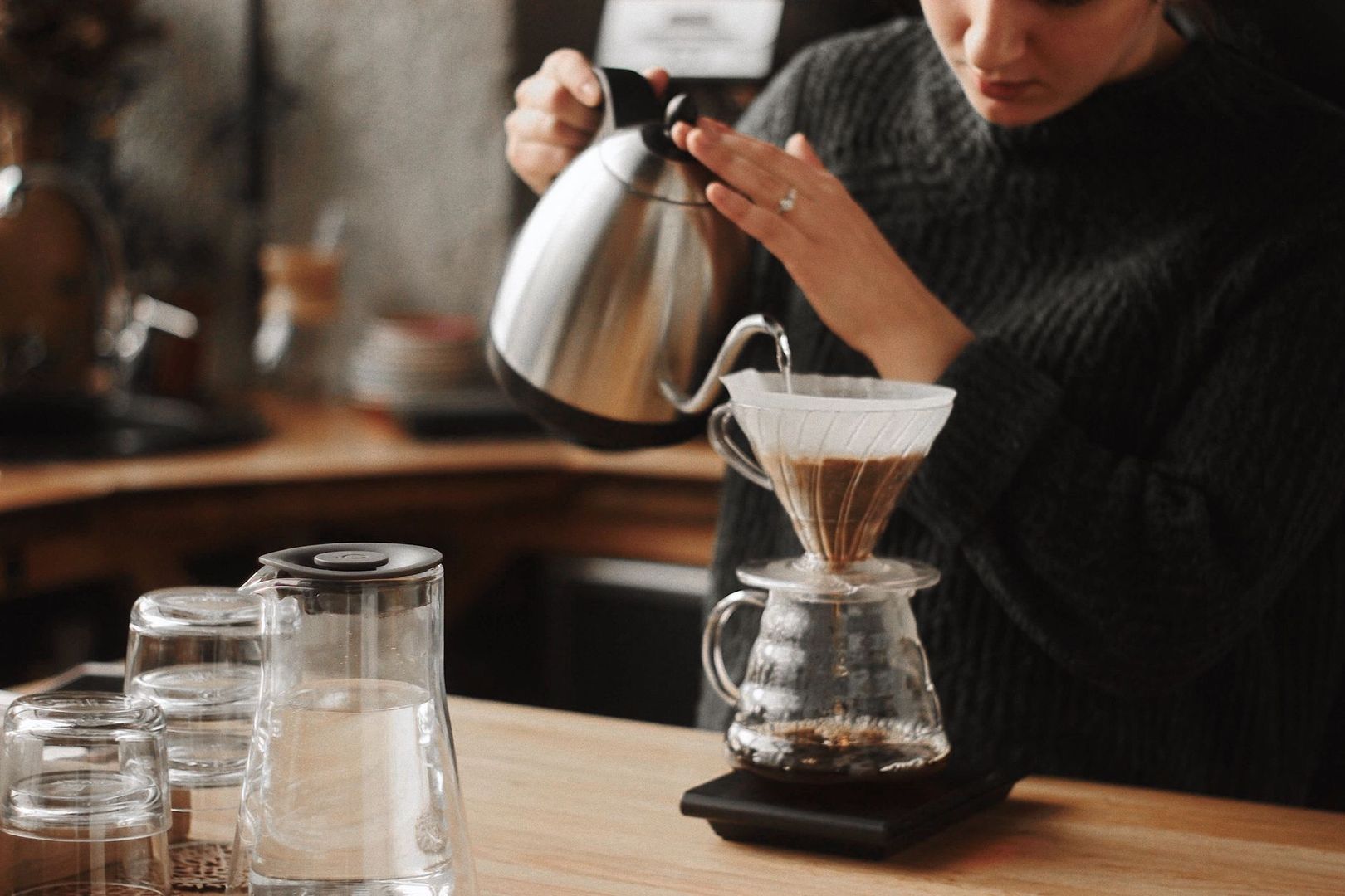 Barista schenkt met een waterkoker filterkoffie in een glazen dripper